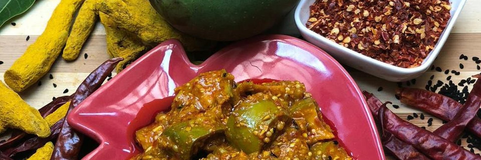 JYOWNAR mango pickle in a ceramic bowl with fresh mango, turmeric and chilli flakes